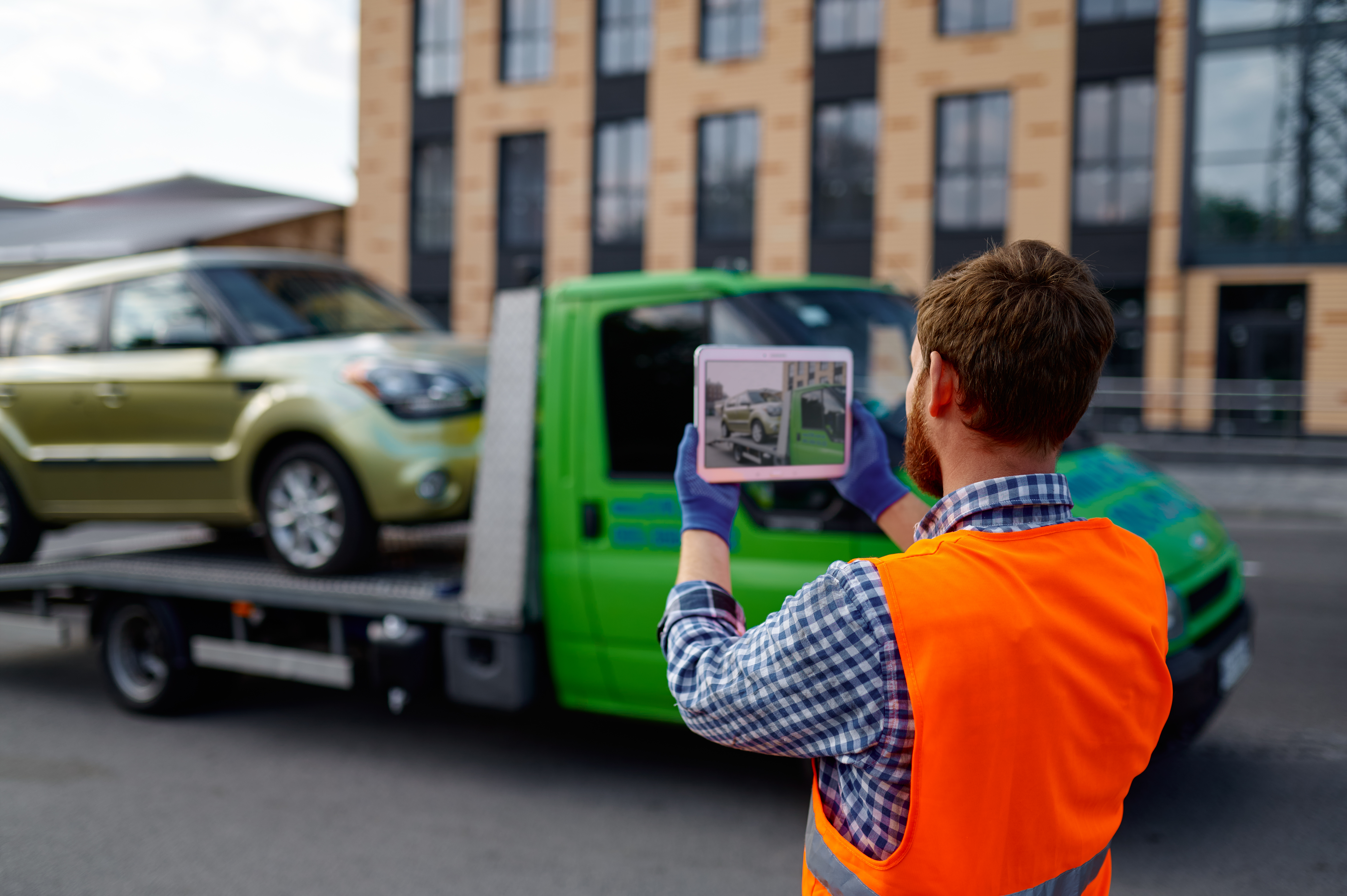 Male tow truck assistant take picture of loaded vehicle. Car insurance. Back view. Selective focus