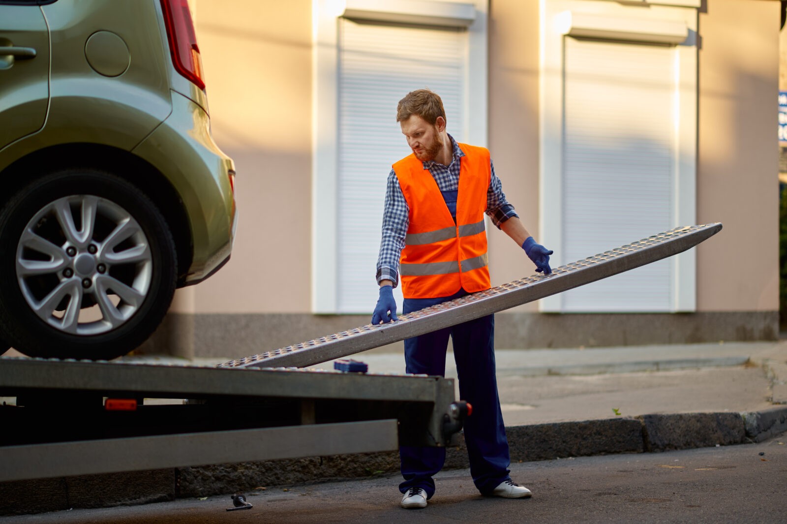 Male road worker in uniform preparing tow truck platform for car loading on city street side